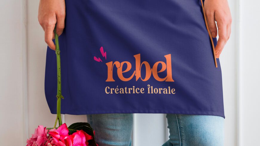 Tissu de tablier violet avec le logo “rebel – Créatrice florale” et un bouquet de fleurs roses tenu à la main.