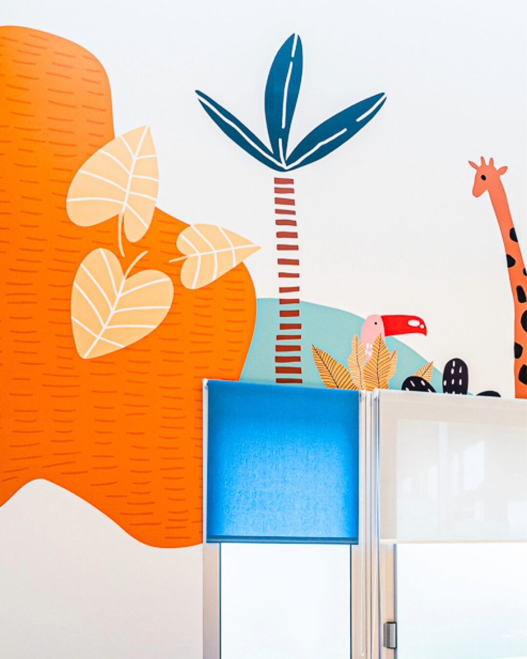 Illustration colorée dans une salle pédiatrique du Centre Kerpape, réalisée par Pois Chiche Design : palmiers, feuilles, toucan et girafe.