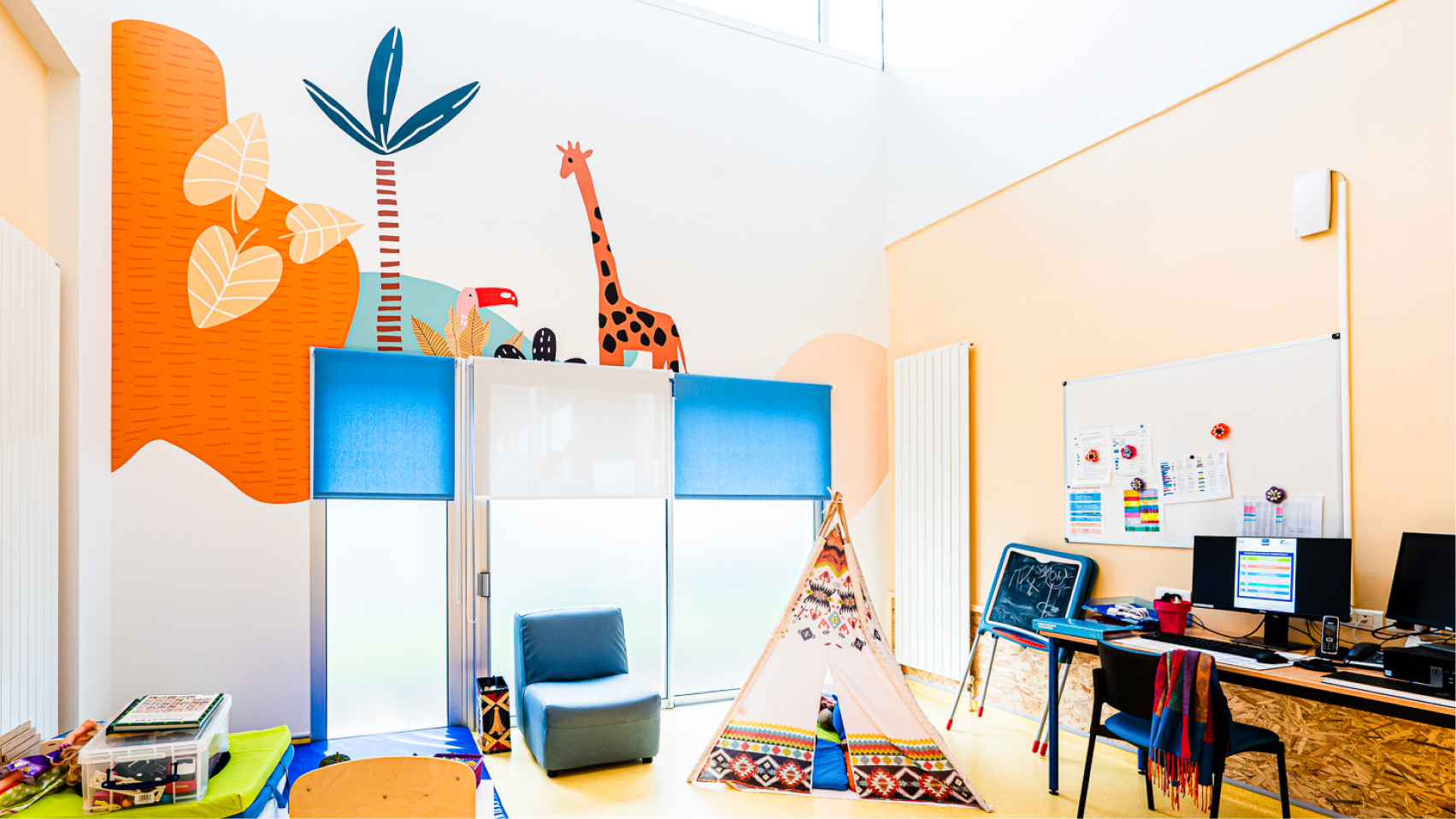 Salle enfant du Centre Kerpape décorée par Pois Chiche Design : fresque colorée avec girafe, toucan, palmiers et formes graphiques.