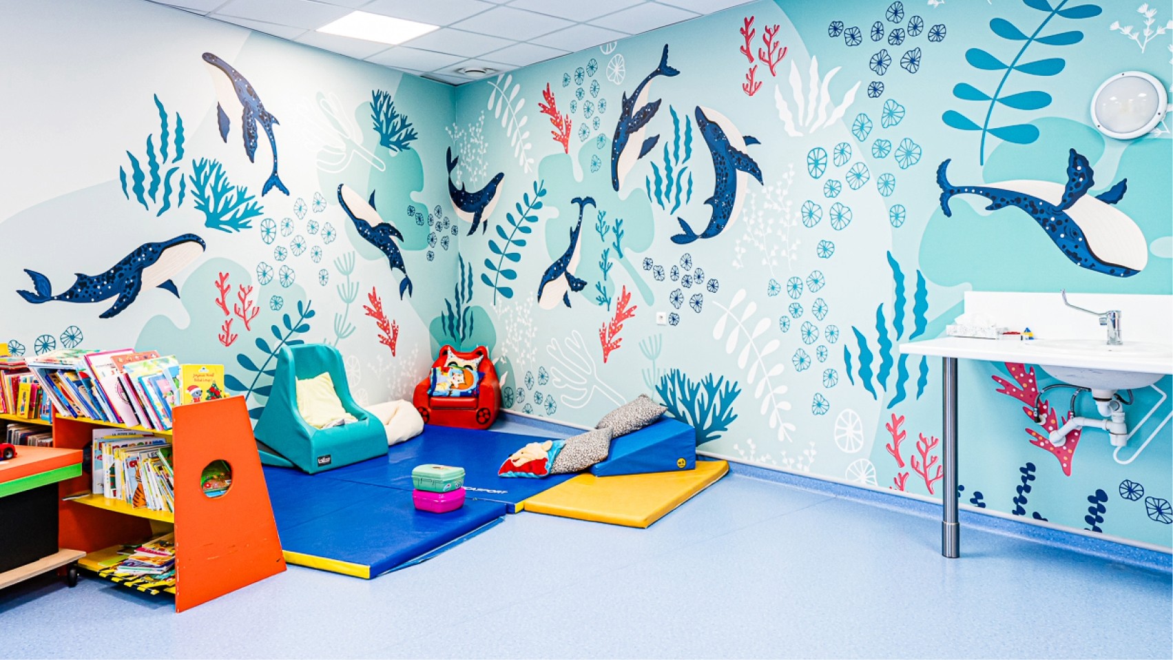 Salle enfant du Centre Kerpape décorée par Pois Chiche Design avec une fresque sous-marine : baleines, algues et coraux colorés.