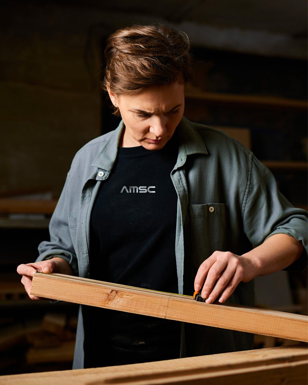 Artisan AMSC mesurant une pièce de bois dans l’atelier — photographie illustrant le savoir-faire en agencement et menuiserie, identité signée Pois Chiche Design.