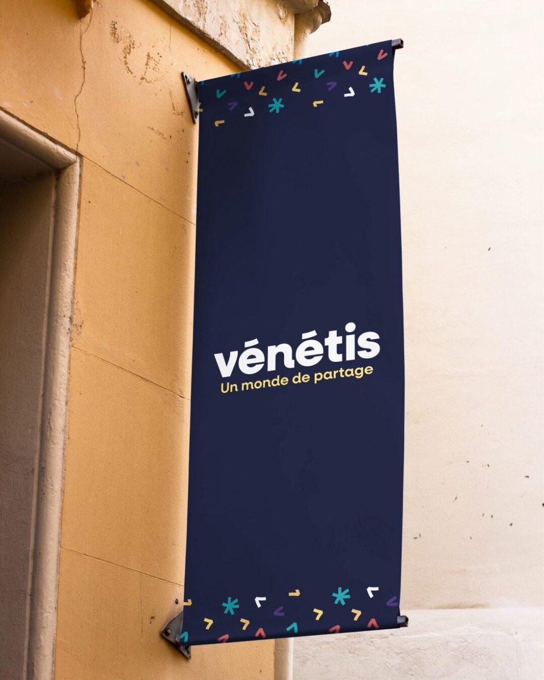 Bâche signalétique Vénétis suspendue sur façade, présentant le logo et le slogan « Un monde de partage », design réalisé par Pois Chiche Design à Lorient.