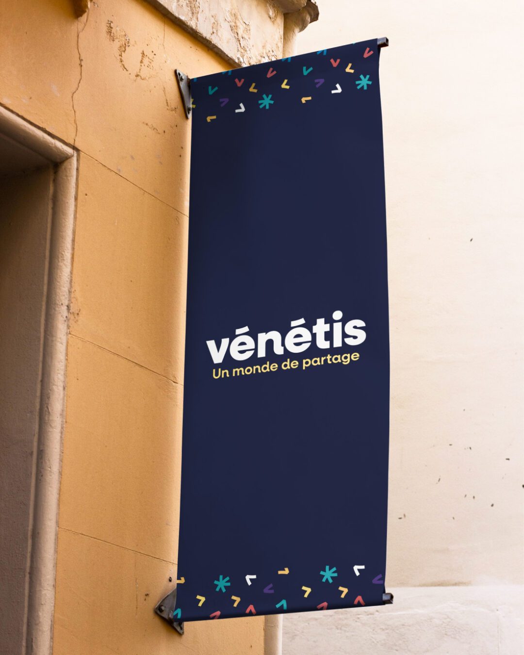 Bâche signalétique Vénétis suspendue sur façade, présentant le logo et le slogan « Un monde de partage », design réalisé par Pois Chiche Design à Lorient.